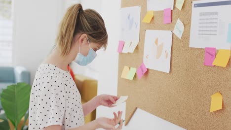 Frau-Mit-Gesichtsmaske-Schreibt-Im-Büro-Auf-Notizzettel