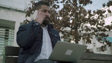 Serious-man-working-with-laptop-and-smartphone-outdoor