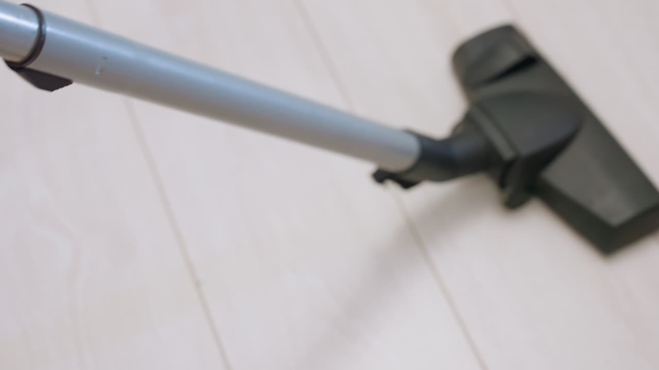 Close up hand view of person adjusting vacuum hose connection, pressing button on gray tube to secure attachment, preparing cleaning equipment for use in modern home environment