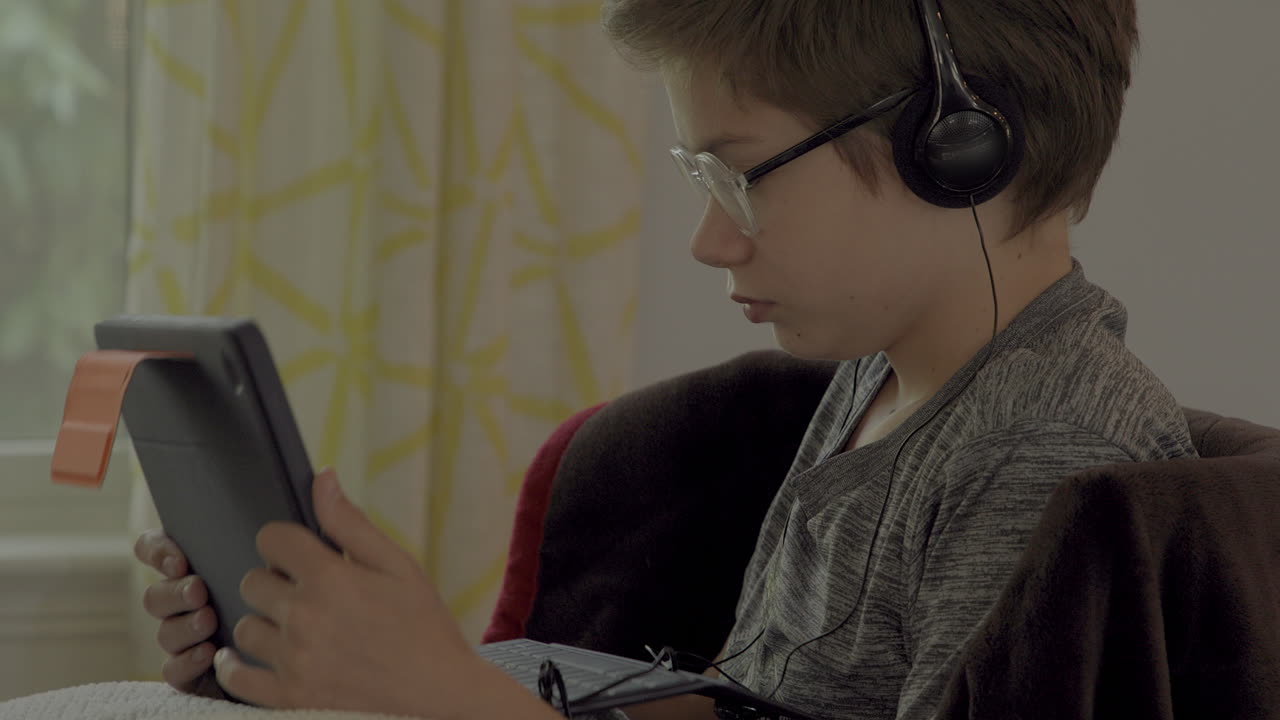 Closeup of a young boy on a tablet and wearing headphones at home in a virtual class