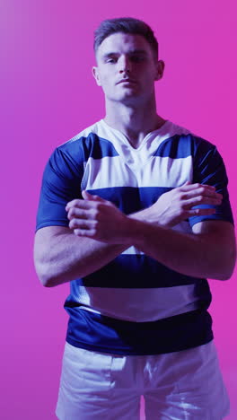 vertikales video von porträt eines kaukasischen männlichen rugby-spielers über rosa beleuchtung