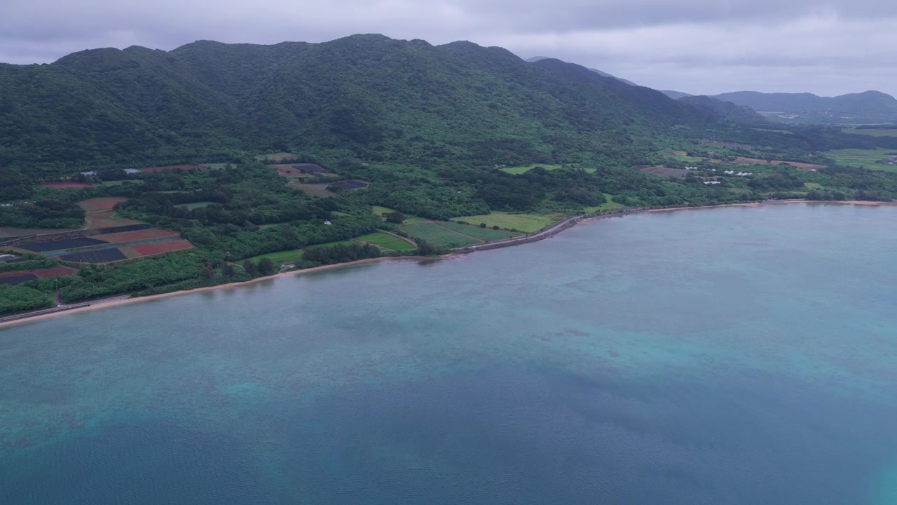 Japonya, Okinawa, Ishigaki Adası'ndaki Nagura Koyu'nun turkuaz kıyı şeridi, tarım arazileri ve ormanlık tepelerinin üzerinde geriye doğru hareket eden yatay hava çekimi