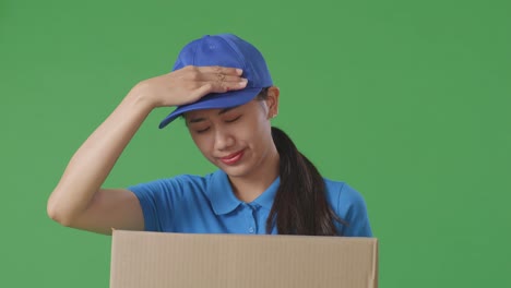 close up of tired asian female courier in blue uniform shaking her head while delivering a carton on green screen background in the studio