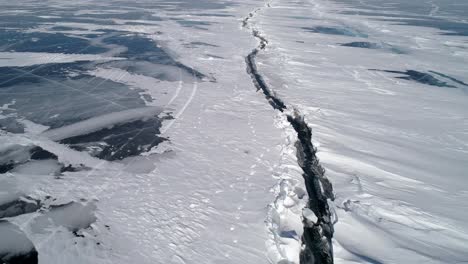 aerial above the huge deep crack on snow covered frozen ice surface of lake baikal. natural landmark. winter landscape. popular touristic destination.