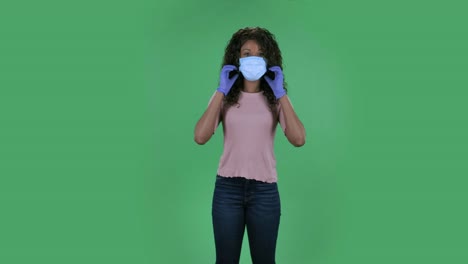 portrait of beautiful african american young woman which is removes medical protective mask breathes air and smiling. redhead with long straight hair in a white blouse on a green screen in the studio. health protection corona virus concept. slow motion