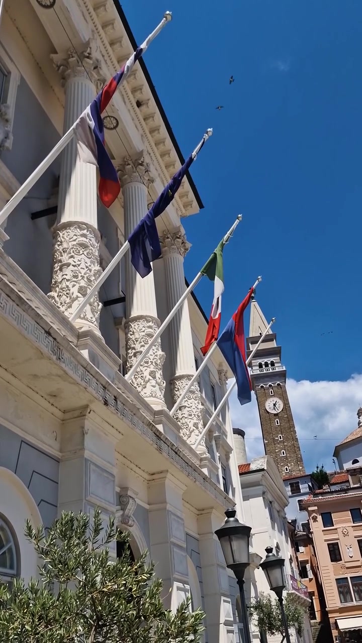 Municipio di Pirano, Slovenia, con bandiere e torre campanaria con orologio veneziano in una calda giornata estiva, vista verticale