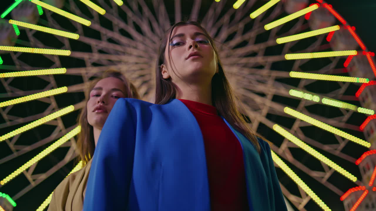 Gorgeous girls look camera at blinking ferris wheel closeup. Two trendy models