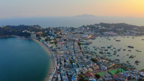 Drone-shot-traveling-to-the-right-above-a-city-built-on-an-isthmus-with-an-harbor-and-a-popular-beach-during-golden-hour