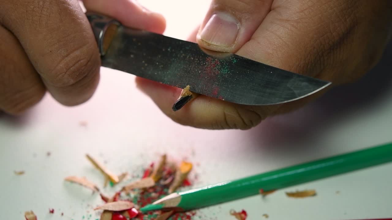 Opptak av hender som sakte spisser en blyant og noen fargeblyanter med en skarp kniv