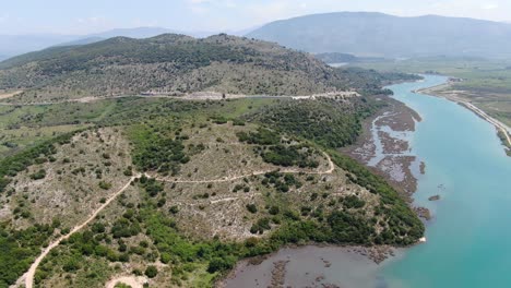 drone view in albania flying over wide river and green landscape next to the sea with mountains on the back