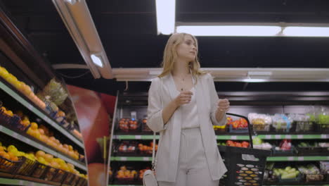 a beautiful woman walks through the supermarket with a basket in her hands looking at the shelves of fruit. buying fresh fruits and vegetables.