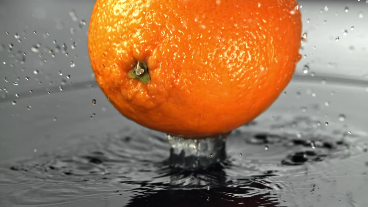 Frisk appelsin falder ned i vand med plask i slow motion