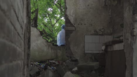 A-man-wearing-a-blue-raincoat-is-sitting-in-a-part-of-a-dilapidated-building