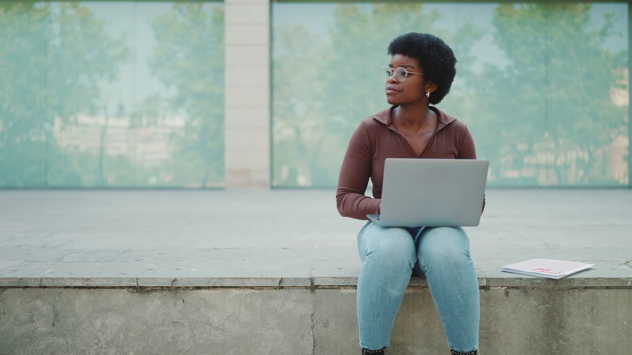 Young curly woman working on laptop outdoors