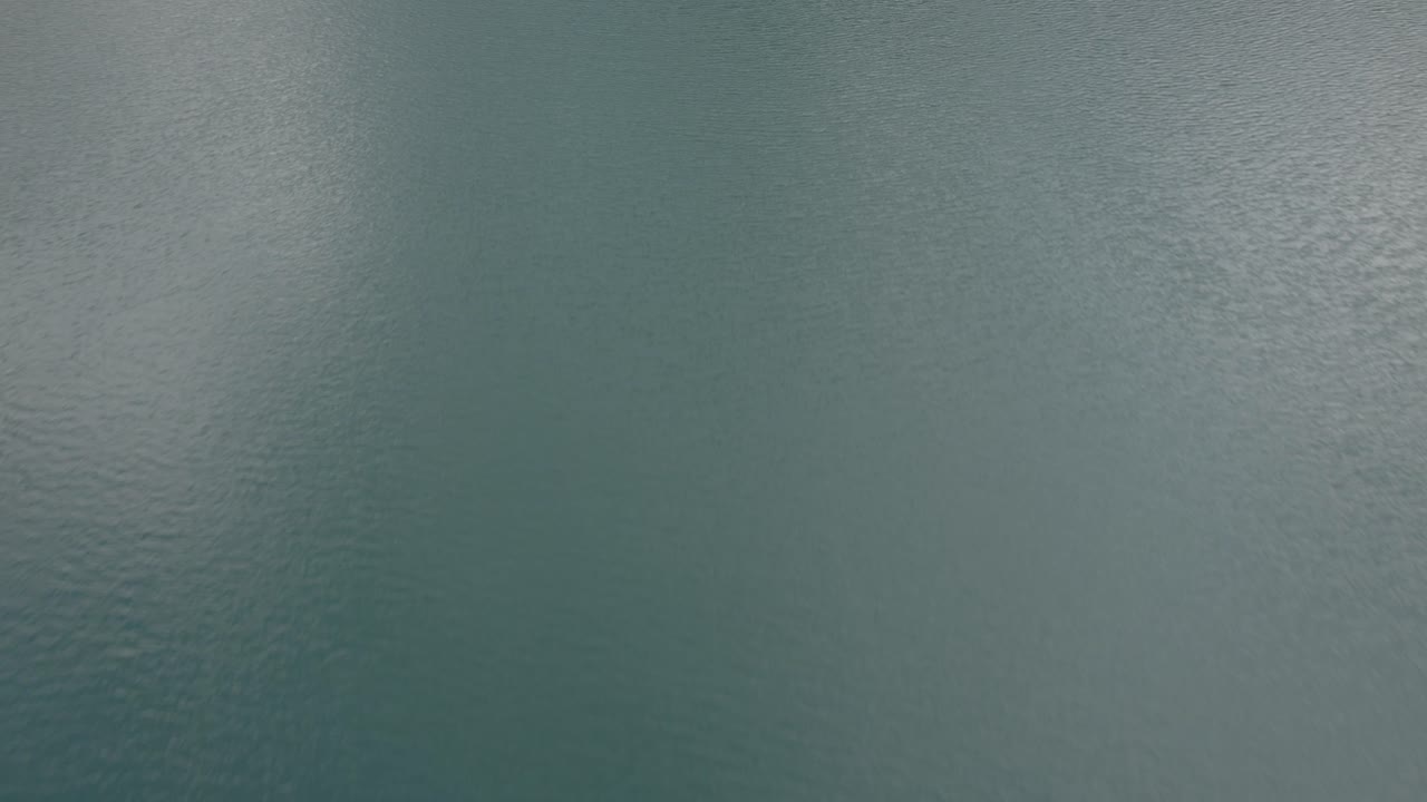 Drone video with descriptive side reverse plane over Braies lake with boats with people rowing and mountains on the horizon
