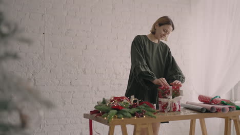 Retrato-De-Una-Chica-Decoradora-De-Un-Envoltorio-De-Regalo-Parada-En-Una-Mesa-Con-Adornos-Con-Papel-De-Regalo,-Ramas-Y-Cintas-Navideñas