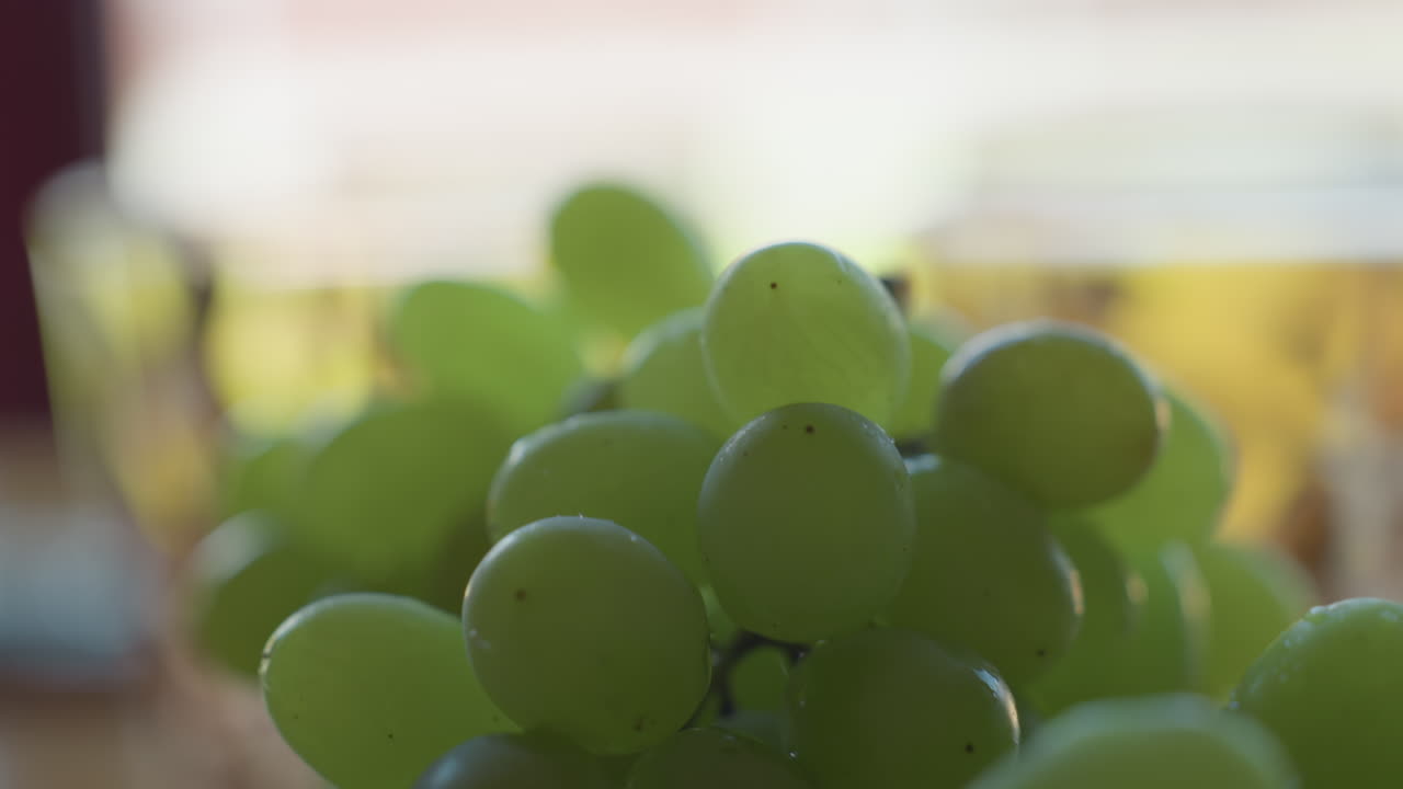 Close up of vibrant green grapes resting on glass plate with bright defocused background, emphasizing freshness and juicy texture of fruit under warm natural lighting in peaceful indoor setting
