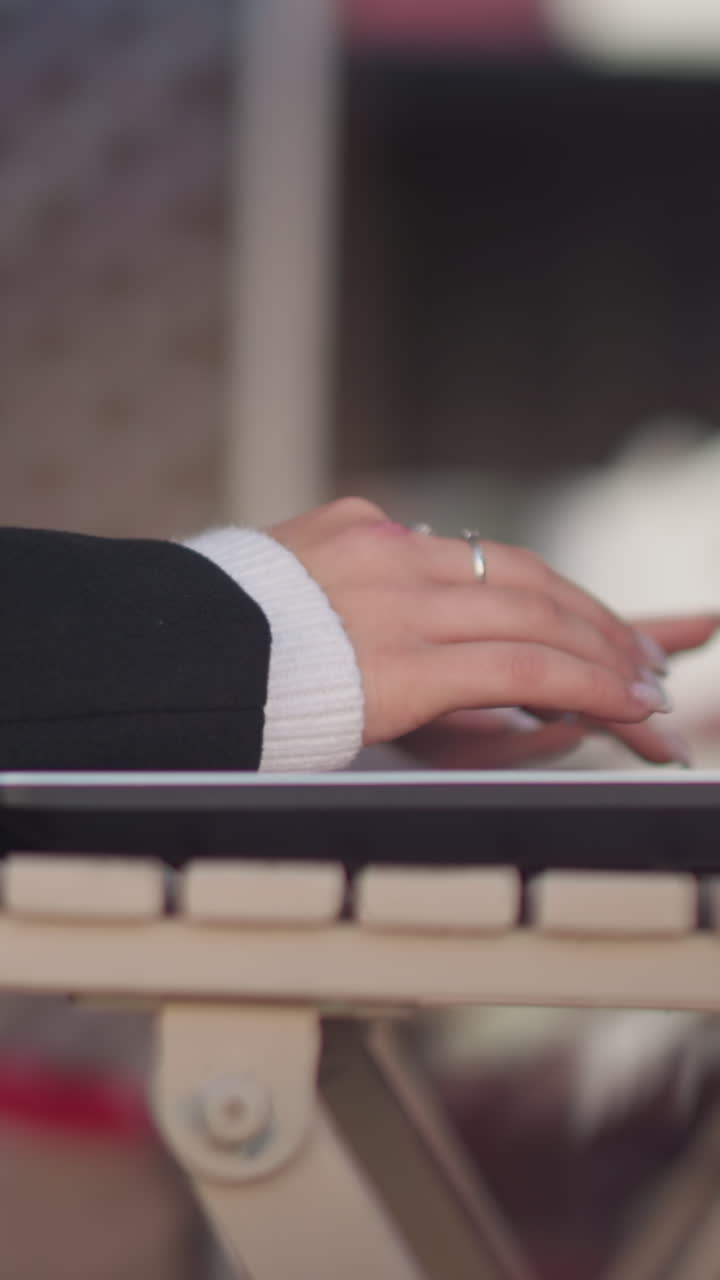 Side view of lady typing on laptop placed on wooden table with polished nails and cozy sweater sleeves, background features blur and subtle glitch effect