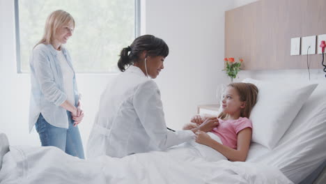 female doctor listens to girls chest whilst visiting mother and daughter in hospital ward