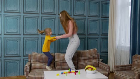 Young-mother-babysiter-and-little-kid-daughter-jumping-dancing-on-sofa-in-modern-house-living-room