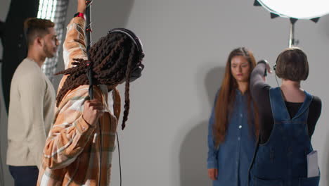 female production assistant uses clapperboard as actors shoot movie or video in studio with sound recordist holding microphone pole