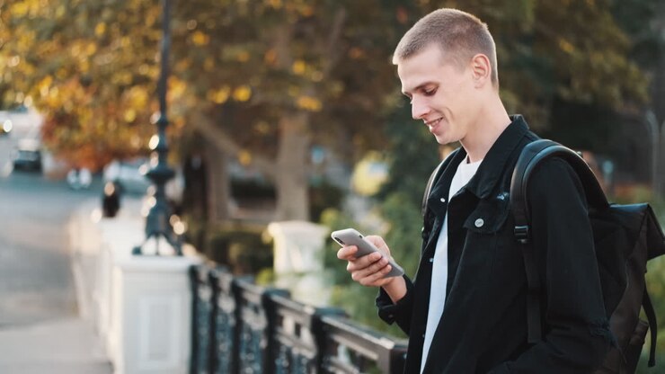 Happy young student using mobile phone outdoors.