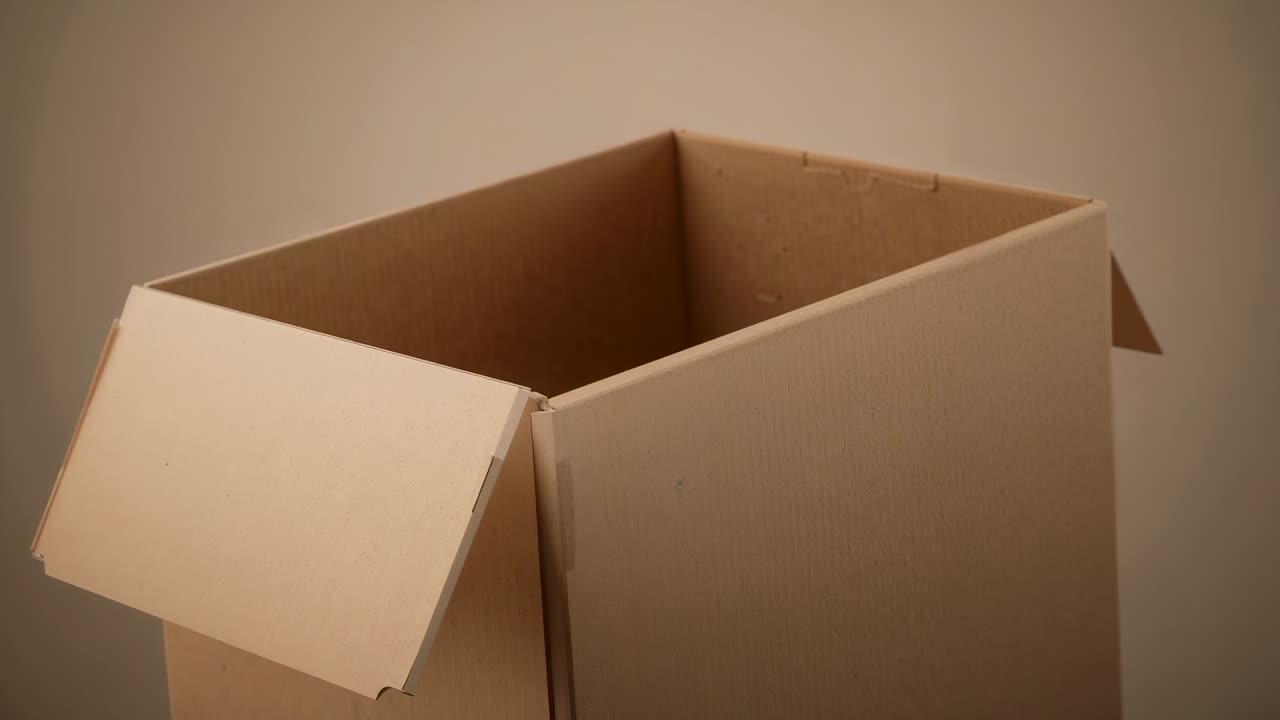 Sitting cardboard box staying empty by neutral beige wall as camera shifts revealing depth