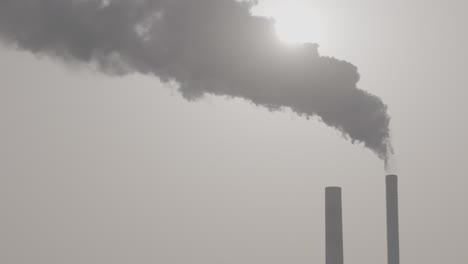 slowmotion shot of industrial smoke from a chimney going up in the air with the sun shining through in the background log