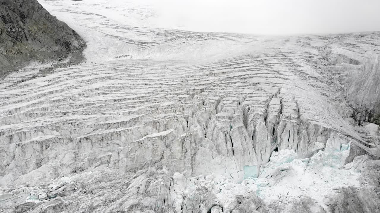 İsviçre'nin Valais bölgesindeki Grimentz yakınlarındaki Moiry Buzulu üzerinde havadan yapılan çekim; bulutlu bir yaz gününde, buzlu yarıkların aşağı kaydırılan görüntüsüyle.