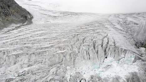 Aerial-flyover-above-the-Moiry-glacier-near-Grimentz-in-Valais,-Switzerland-with-a-pan-down-view-of-the-icy-crevasses-on-an-overcast-summer-day