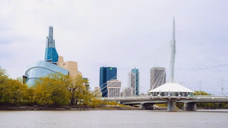 Heller,-Bewölkter-Tag-über-Dem-Ufer-Des-Assiniboine-Red-River-In-Der-Innenstadt-Von-Winnipeg,-Manitoba,-Kanada,-Mit-Dem-Kanadischen-Museum-Für-Menschenrechte-Und-Der-Provencher-Bridge-Im-Hintergrund