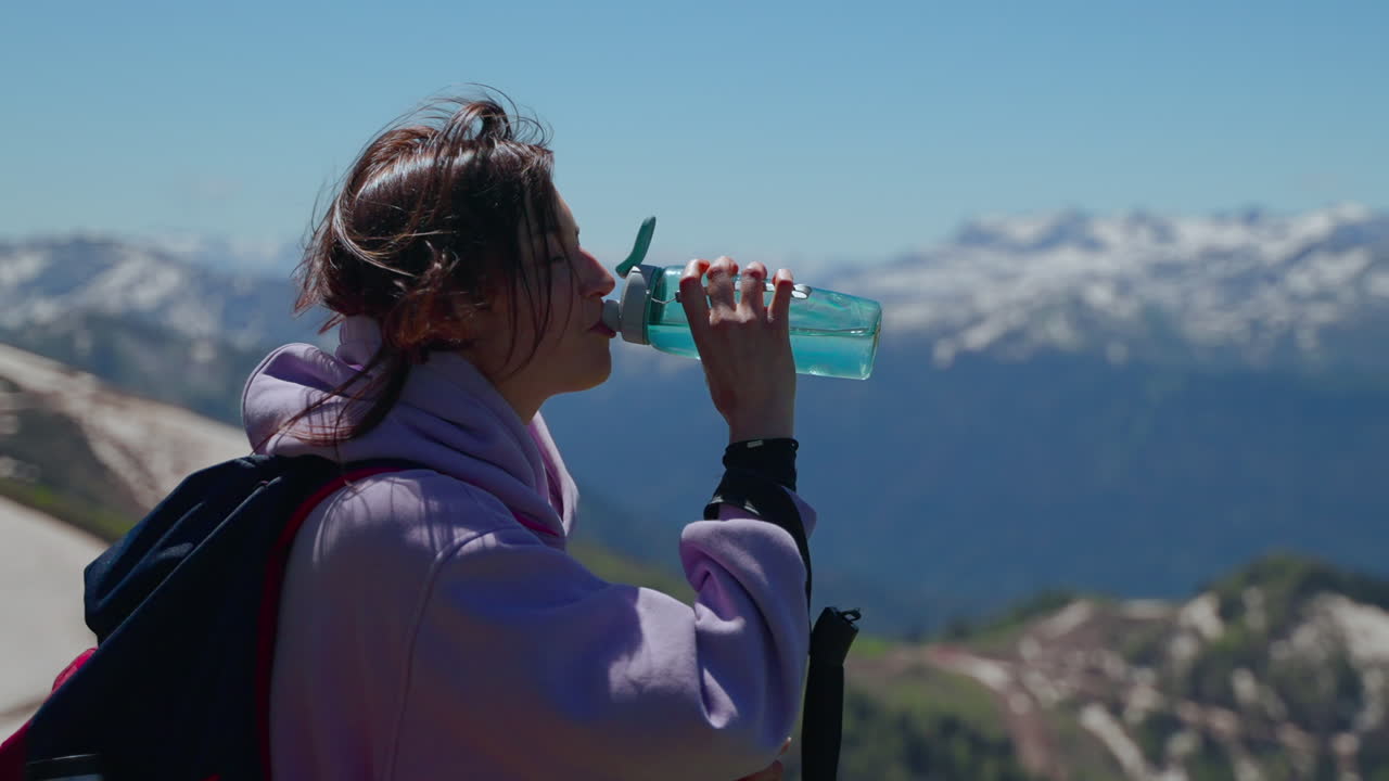 mujer caminando y bebiendo agua en las montañas