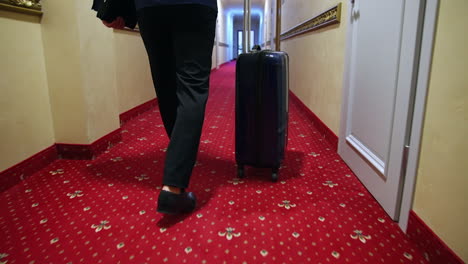 traveller with suitcase in hallway. man moving along the hotel corridor with a travel bag. man pulling his luggage. rear view.
