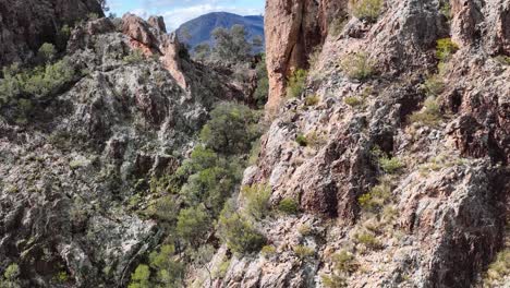 camera slowly pans across rugged rock formations and sparse vegetation in bright daylight, revealing the dramatic landscape of warrumbungle national park, new south wales