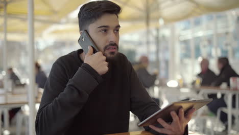 Focused-young-man-using-digital-tablet-and-smartphone-in-cafe