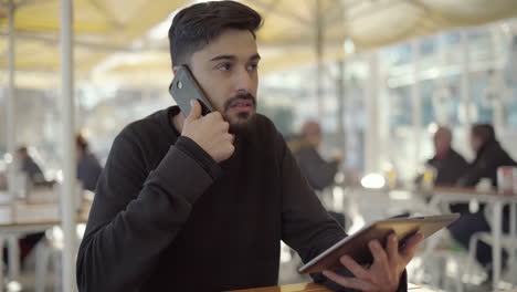 Focused young man using digital tablet and smartphone in cafe