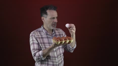 an older male in a plaid shirt, holding a white egg and a carton of brown eggs, with a serious, contemplative look