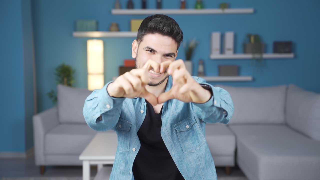 사랑에 빠진 젊은 남자와 긍정적으로 카메라를 바라보며 심장 기호를 하고 있습니다.