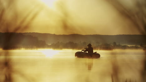 vista lejana del anciano en un sombrero navegando en un bote en el lago al atardecer