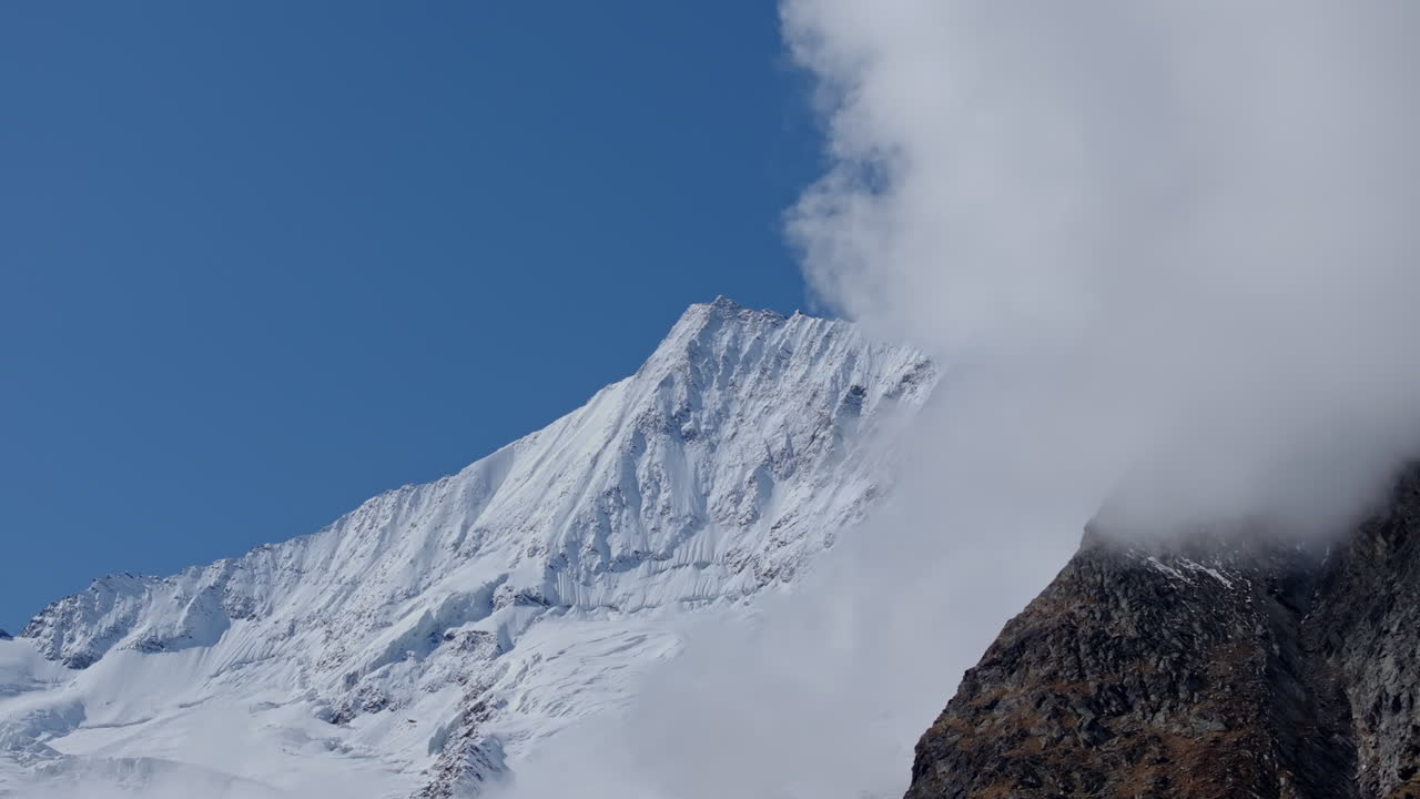 Stunning aerial footage of Saas-Fee in autumn. Golden forests surround the alpine village, nestled in the Swiss Alps. Vibrant fall colors and majestic peaks highlight the beauty of the season.