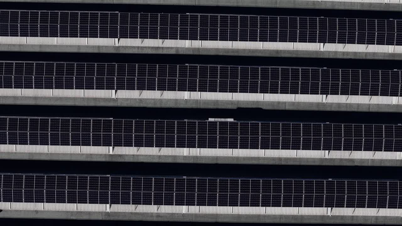 Photovoltaic solar panels on industrial rooftop arranged in parallel rows forming geometric pattern, static top down aerial shot