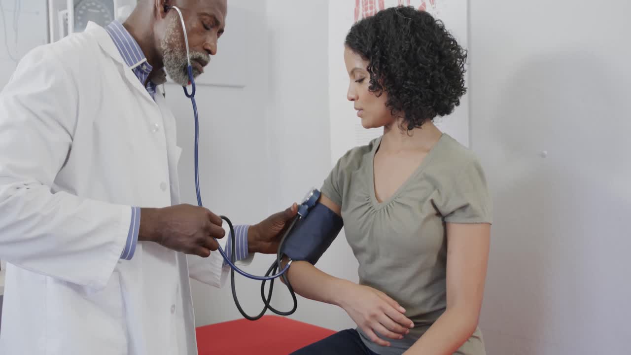 Diverse male doctor examining female patient, measuring blood pressure, slow motion
