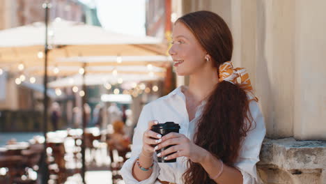 a young woman with red hair smiles while holding a coffee cup on the street