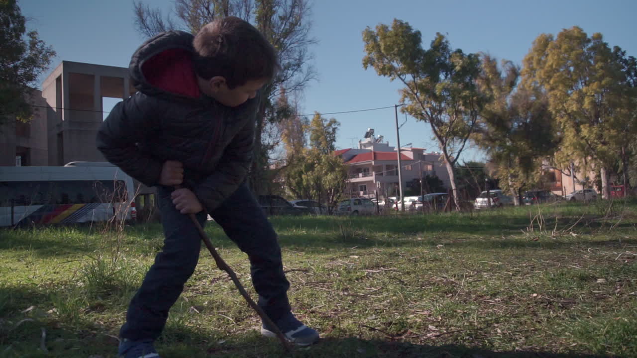 medium shot of toddler in the fields digging with a wooden stick