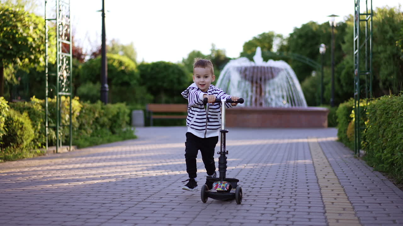 Energetic Caucasian boy runs pulling his scooter. Active three-year-old toddler having fun in the park in summer.