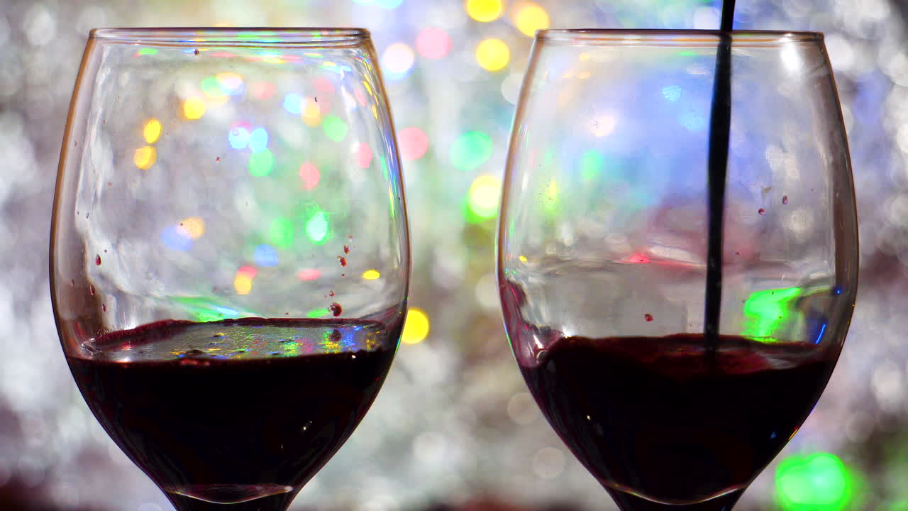 Two wine glasses red wine poured in on colorful bokeh and silver blanket close up in a romantic intimate atmosphere