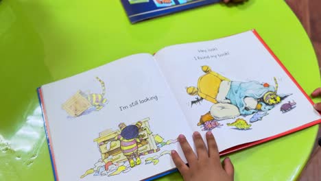 child flips through a colorful illustrated storybook on a green table, promoting early reading, storytelling, and literacy development. perfect for educational and family-themed footage.