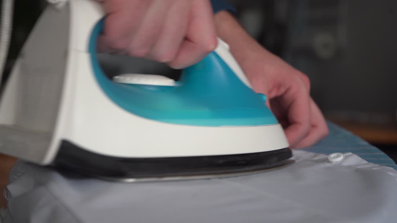 Ironing board close-up: Man irons white dress shirt, depth of field