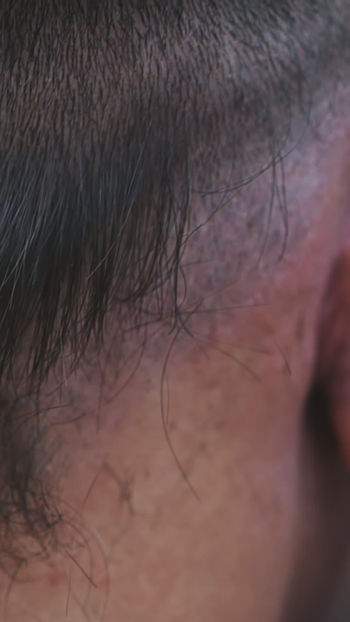 CU, slow motion: skilled hairstylist shaves black hair on male client head with modern clipper in barbershop on black background backside close view