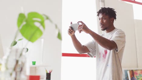 artista afroamericano que toma una foto de su pintura con un teléfono inteligente en un estudio de arte